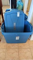 Blue Rubbermaid storage totes stacked with lids visible, placed on a tiled floor.