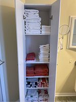 Full view of tall white cabinet with shelves filled with multiple stacks of towels in various colors and sizes.