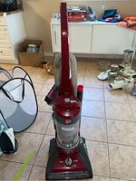 Full view of the red upright Hoover vacuum cleaner in a room setting showing its overall condition and accessories.