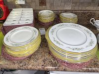 Stack of dinner plates, side plates, cups and saucers arranged on countertop.