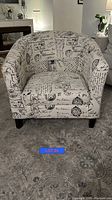 White fabric accent chair with black postal and script print in a barrel back shape.