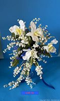 Front angled view of the artificial bouquet showing Lily of the Valley and Iris flowers on blue background