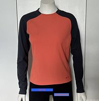 Front view of long sleeve athletic top on mannequin showing black sleeves and orange body.