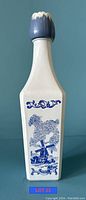 Tall white ceramic Vandermint liquor bottle with blue windmill and floral design, blue ceramic stopper shaped like a flower bud on top.