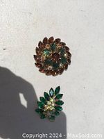 Two vintage-style costume jewelry brooches with colorful rhinestones on a white surface