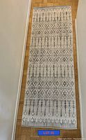 Top view showing full length of rectangular runner rug with geometric diamond and linear pattern in black on beige.