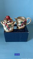 Photo of Fitz and Floyd Christmas cream and sugar bowls, set on original box, showing detailed holiday decoration.