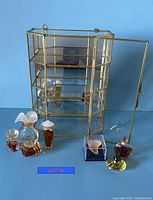 Glass and brass curio with open door and 7 fragrance miniature bottles in front on blue background.