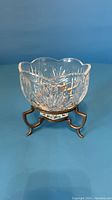 Side view of a clear glass decorative bowl with detailed etched floral patterns on a brass stand with four legs.