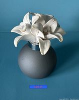 Gray round diffuser with white ceramic flower top against blue background, showing hairline crack on one petal.