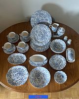 Photo showing entire dinner set on table, includes plates, cups, saucers, serving pieces in blue floral pattern.