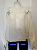 Front view of the off-white women's top on a mannequin showing long sleeves with elastic cuffs and ruffled shoulder detail.