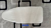 Top view of portable ironing board with white fabric cover on patterned carpet
