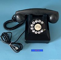 Photo of vintage black rotary phone by Northern Electric with coiled handset cord and rotary dial with numbers and letters.