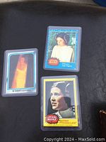 Three Star Wars collectible cards displayed on a dark surface, showing character Princess Leia and Darth Vader, each in clear protective sleeves.