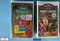 Photo of two factory sealed Disney VHS tapes from the Masterpiece Collection: The Little Mermaid and Robin Hood, showing front cover artwork and original price stickers.