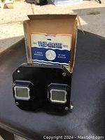 Photo of black vintage View-Master viewer next to original box with one visible reel inside labeled '7 More Wonders of the World'