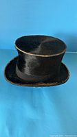 Front and side view of the vintage black top hat with some wear and gold trim visible.