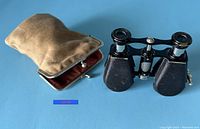 Vintage opera glasses next to original velvet case on blue background showing the front view of glasses and case details