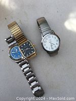 Photo of three wristwatches: one gold-tone with black face and two silver-tone, one with a white face and one with a blue face, all metal linked bands
