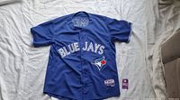Front side of the blue Toronto Blue Jays jersey with 'BLUE JAYS' text and logo patch showing. Size tag visible.
