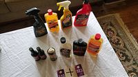 Top-down view of various car detailing products on white cloth including spray bottles, liquid cleaners, waxes, small bottles, Canadian flags, and tie down system parts.