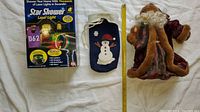 Photo of Star Shower Laser Light box, snowman bag, and St. Nicholas statue with measuring tape for size reference