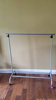 Front view of the extendable metal and plastic clothes rack on casters showing overall frame and adjustable top hanging bar.