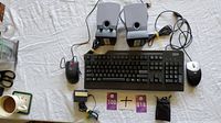 Photo of IBM keyboard, two wired computer mice IBM (black) and HP (white/black), pair of small gray Harman/Kardon speakers, power adapter and two purple floppy disks on white tablecloth.