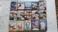 Multiple DVD cases showing a variety of movies and workout DVDs arranged on a white fabric surface.