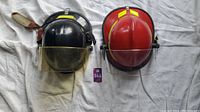 Front view of black and red fire helmets placed side by side showing visors and neck flaps.