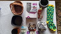 Photo showing various miscellaneous household items laid on table including baskets, black plant pots, bright sock, jar candle, reusable ice packs, small blanket, and cookie cutters.
