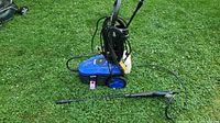 Blue Simoniz 1600 pressure washer unit on grass with power cord and pressure hose wound around the handle, one pressure wand laid flat beside it