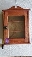 Front view of the vintage wooden curio cabinet showing glass door, brass clasp, and decorative top.