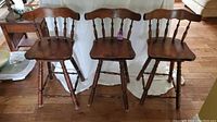 Front-facing view of three wooden swivel bar stools arranged in a row showing overall shape and condition.