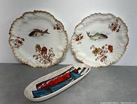Front view of two antique Limoges fish plates and one hand-painted MCM bowl arranged next to each other on gray surface.