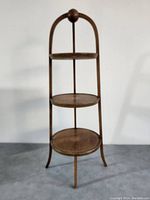 Front view displaying the three circular shelves and the curved leg structure topped with a ball finial.