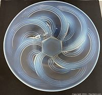 Top view of opalescent glass bowl showing geometric swirl pattern with hexagonal center, resting on black background.