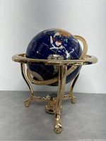 Front angled view of the globe showing the blue lapis lazuli gemstone surface with country outlines and the polished brass stand with three curved legs.