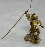 Full view of brass Nezha statue on cloud base holding a long pole weapon with intricate details on armor and weapon.