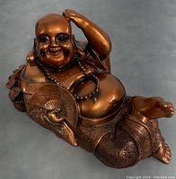 Front angle showing the reclining Happy Buddha statue in brown resin with detailed texture on pants and smiling face.