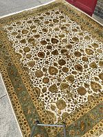 Rug laid flat to show overall ivory field with multicolored floral vine pattern and green border.
