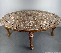 Front angled view of oval coffee table showing detailed bone inlay on tabletop and one leg.