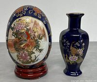 Front angle showing the decorative egg on wooden base and the blue vase with floral bird designs