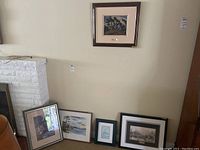 Overview of five framed prints arranged against wall near fireplace, shows various sizes and frame styles.