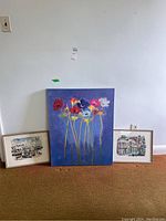 Full view of three art pieces against a wall: one large floral canvas in center, two smaller framed prints on either side.
