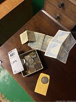 Overall collection of paper money and coins in a small box on a wooden surface.
