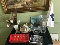 Five Auteuil lead crystal wine glasses, Mikasa wine set in box, milk glass style vase, punch bowl with glasses, and two fan flags on black cloth under a painting