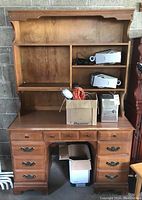 Wood double pedestal desk with hutch, drawers and shelves, showing some clutter on desk surface and shelving. Visible damage on front top edge.