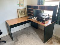 Full view of L-shaped corner desk with attached shelving hutch in office room. Contents on desk and shelves visible but not included.